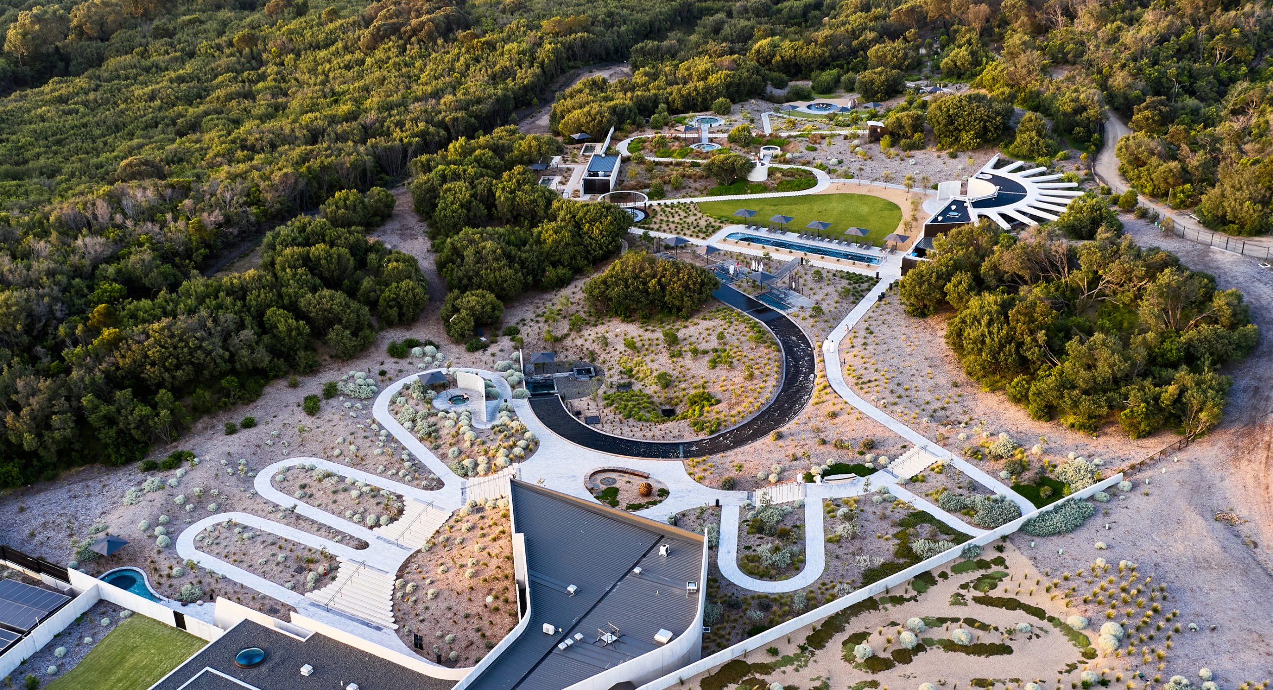 A photo of Alba Thermal Springs from above taken by a drone - the photo shows the buildings designed by architect Hayball nestled amongst the endemic landscape designed bt landscape architect Mala - the photo includes many of the 32 mineral springs that are connected by serpentine paths that encourage guests to wander, explore and be pleasantly surprised.